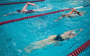 Three adults swimming freestyle in two lanes of a pool.